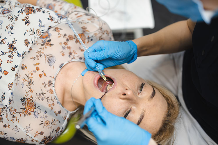 Clínica Dental Andrea Compte, tu Centro Odontológico especializado. Cirugía bucal en Vinaròs. Doctor realizando inyectando anestesia a la paciente para realizar la cirugía.